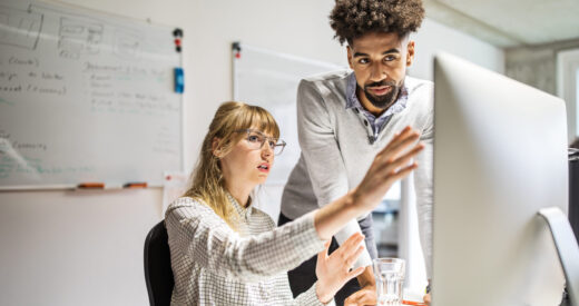 Multi-ethnic businesswoman and businessman discussing over computer at desk in creative office