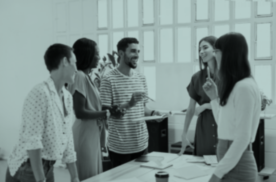 Diverse group of younger professionals talking around a conference room table.