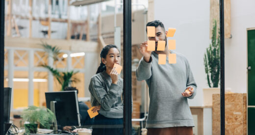 Colleagues discussing while sticking adhesive notes on glass wall in office