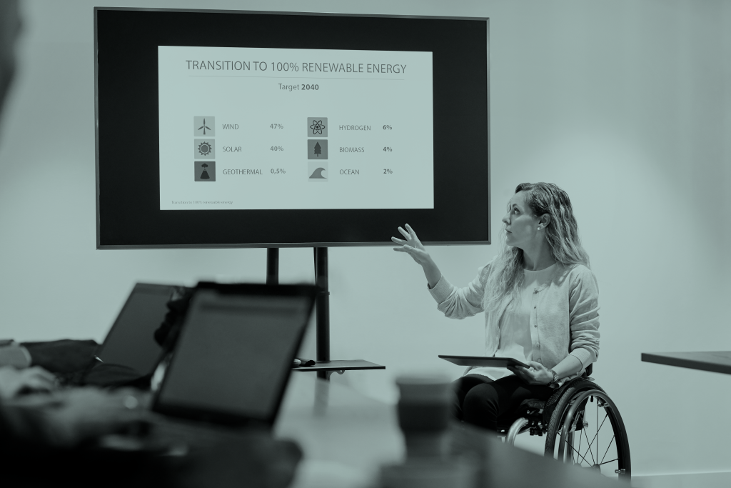 Confident businesswoman on wheelchair explaining presentation. Disabled female executive is gesturing while looking at screen. She is in smart casuals at board room in office.