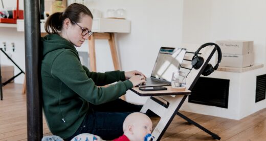 mother working from home on a laptop while watching her toddler beside her