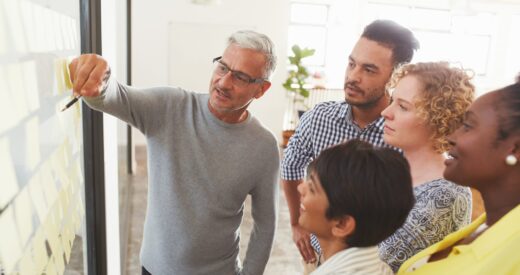 Mature businessman and his diverse team brainstorming with yellow adhesive notes on a glass wall in a bright modern office