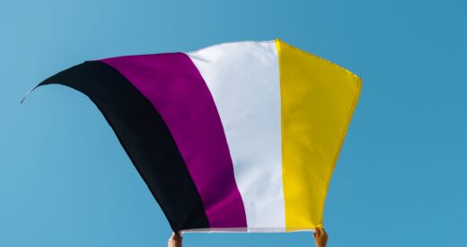 closeup of a young person, seen from behind, waving a non-binary pride flag on the air