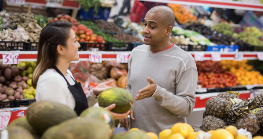 Latinx man in fruit section of supermarket with shop worker helping him