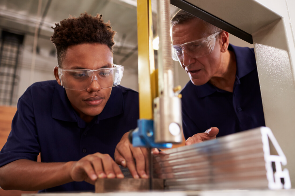 Carpenter Training Male Apprentice To Use Mechanized Saw