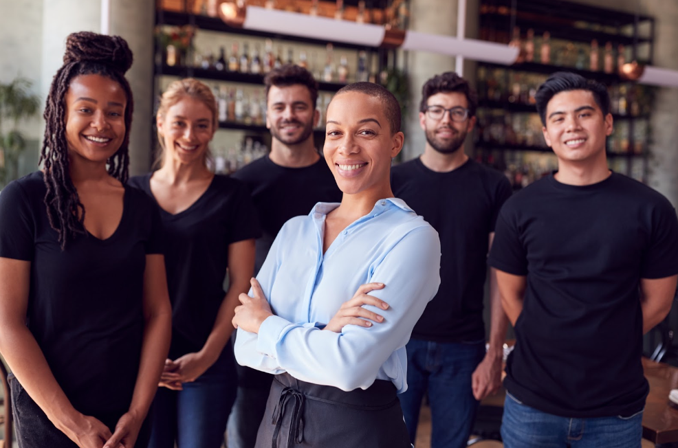 Portrait Of Female Owner Of Restaurant Bar With Team Of Waiting Staff Standing By Counter