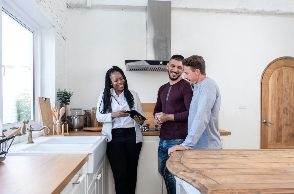 Black female real estate agent in kitchen showing gay couple around new house