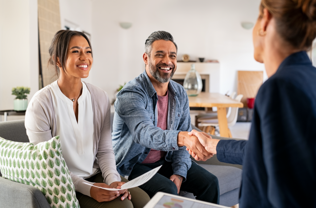 Mature indian man shaking hands with financial advisor at home. Happy smiling couple greeting broker with handshake at home. Multiethnic mid adult man and hispanic woman sealing a contract.