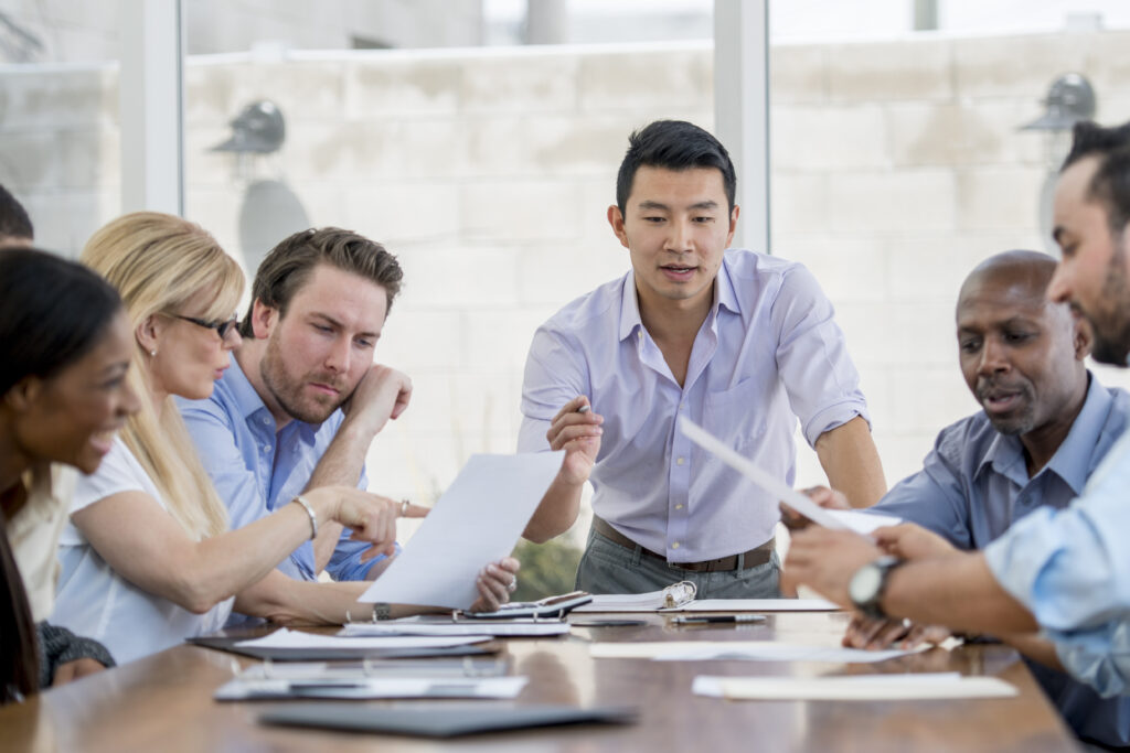 An associate is giving a presentation in the boardroom to a multi-ethnic group of business professionals.