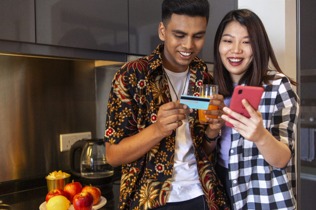 Couple from different ethnic using credit card wirh mobile phone, doing online transaction in house kithen