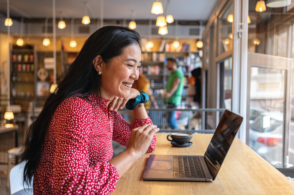 A modern young woman of Asian ethnicity, having a video call via laptop, at the modern and cozy cafeteria