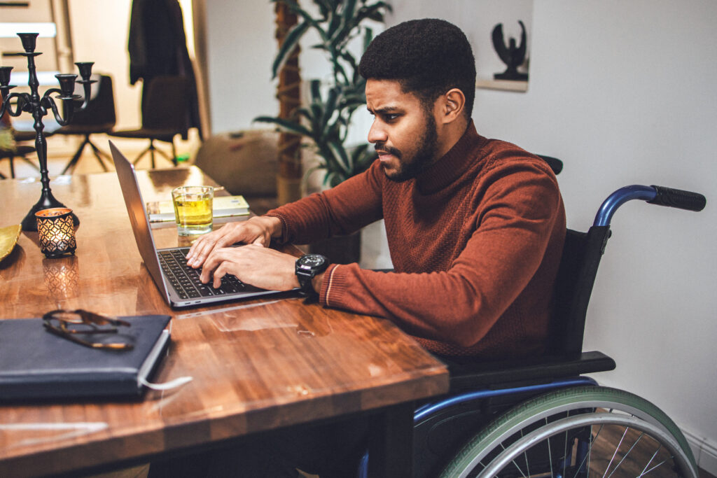 Disabled young African-American male meeting the deadline working at home using laptop.