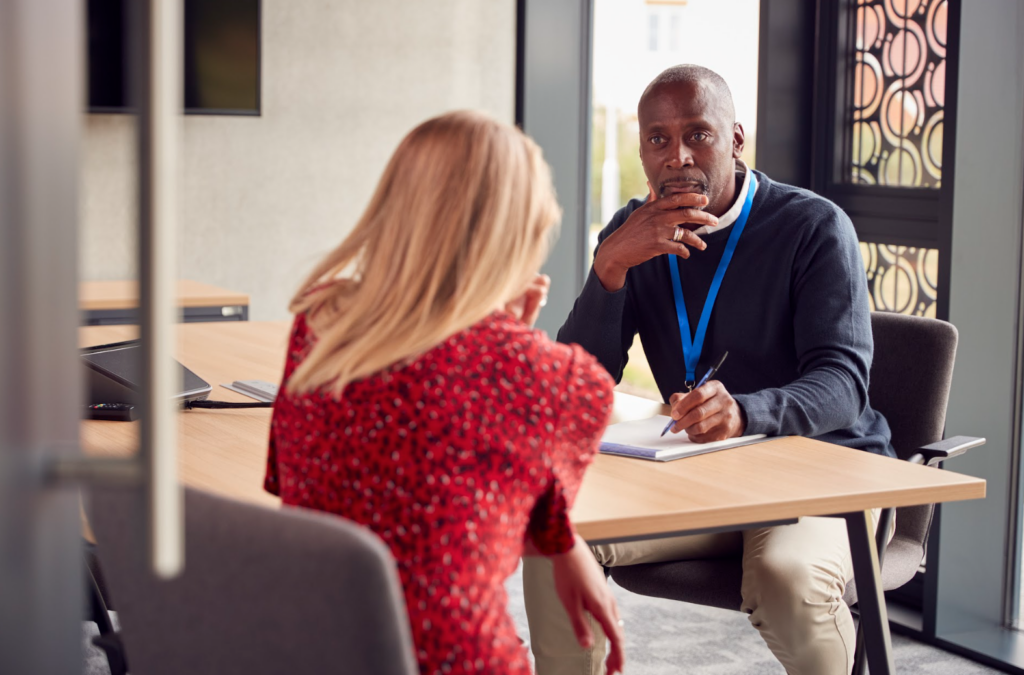 man listening as he has a conversation with a woman at a desk