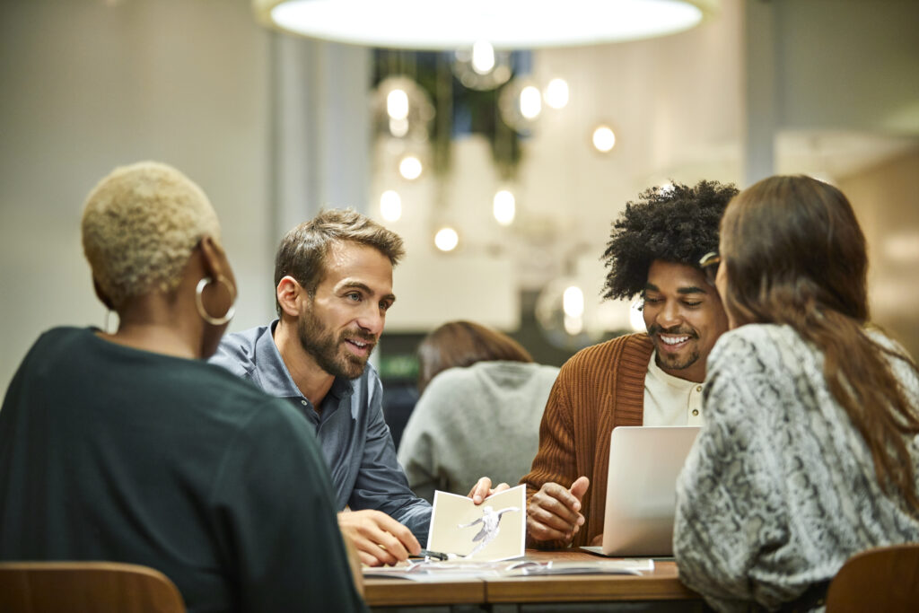 Multi-ethnic business professionals discussing at desk. Male and female coworkers are working in office. They are in meeting.