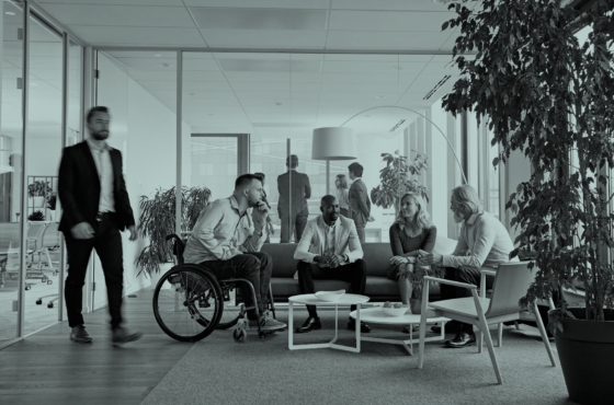 Stock image of diverse colleague collaborating in an open office space. One employee is using a wheelchair