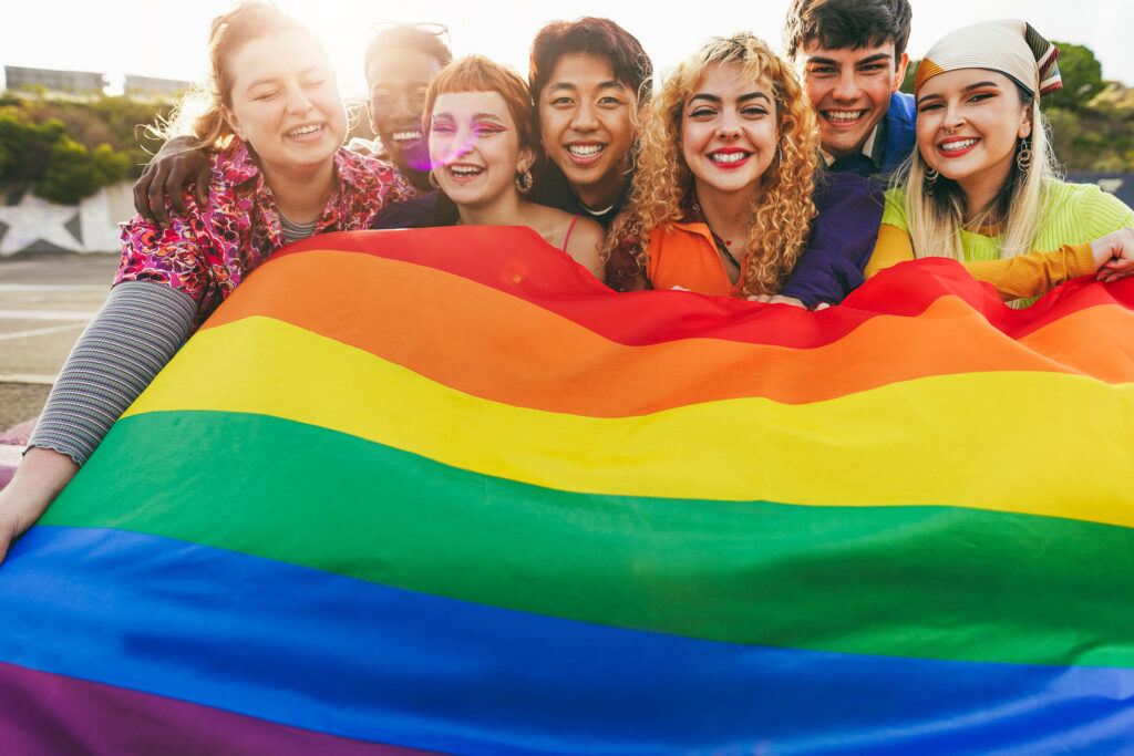 Young diverse people having fun holding LGBT rainbow flag outdoor