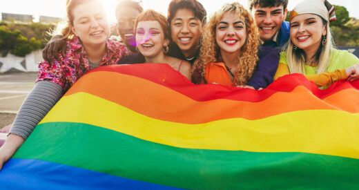 Young diverse people having fun holding LGBT rainbow flag outdoor