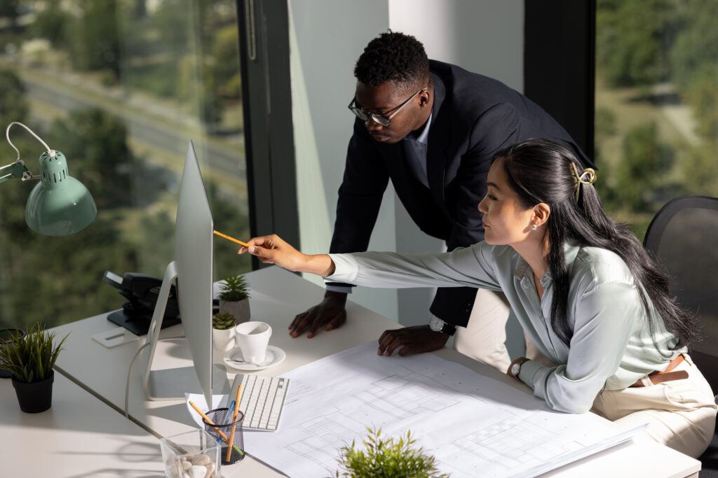 High angle view of a diverse group of architects, young African American man and his female colleague of Mongolian ethnicity working together as a team in their office, drawing some schematics and exchanging ideas