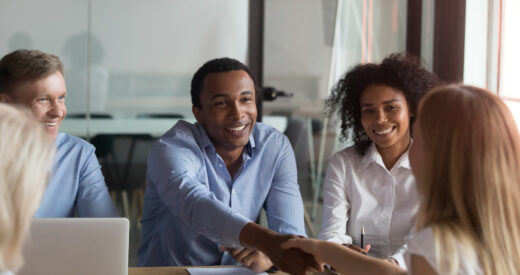 Successful diverse teammates sitting at boardroom, company head shaking hands with millennial specialist woman businesspeople ready to start conference discuss financial report planning future goals