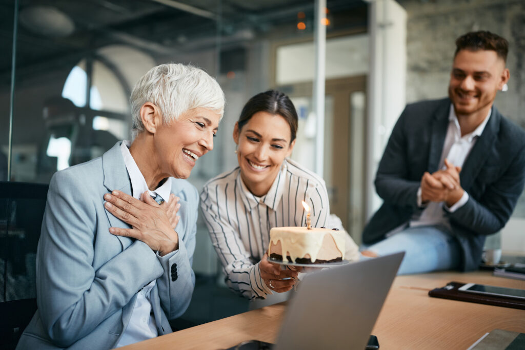 Senior CEO feeling grateful while her coworkers are surprising her with a cake for International Women's Day in the office.