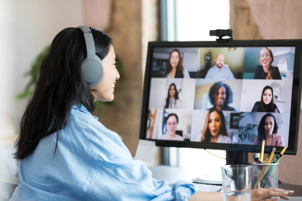 The mid adult female student wears her Bluetooth headphones as she joins the multi-ethnic group of students for a virtual college class.