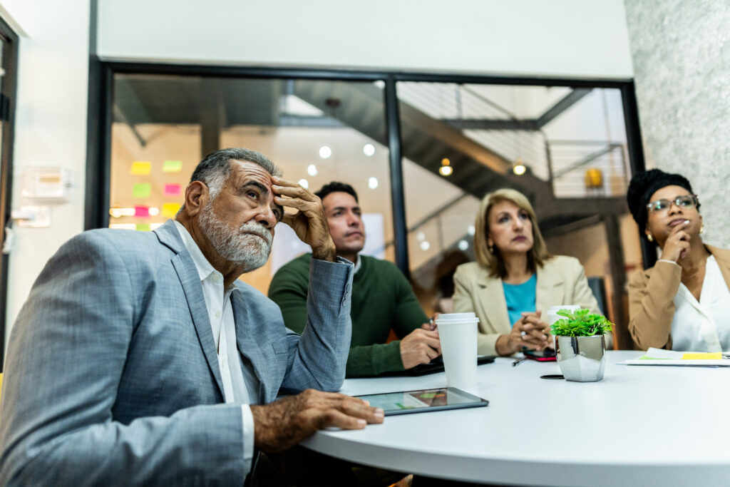 Worried senior businessman listening presentation with coworkers during business meeting at office