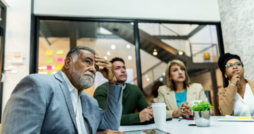 Worried senior businessman listening presentation with coworkers during business meeting at office