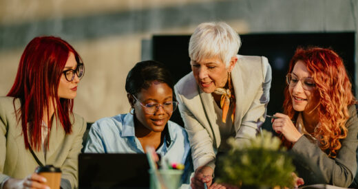 Senior businesswoman is standing at boardroom with her multicultural team and tutoring them. Mature female mentor is teaching her interracial team new business strategies and analyzing data with them.
