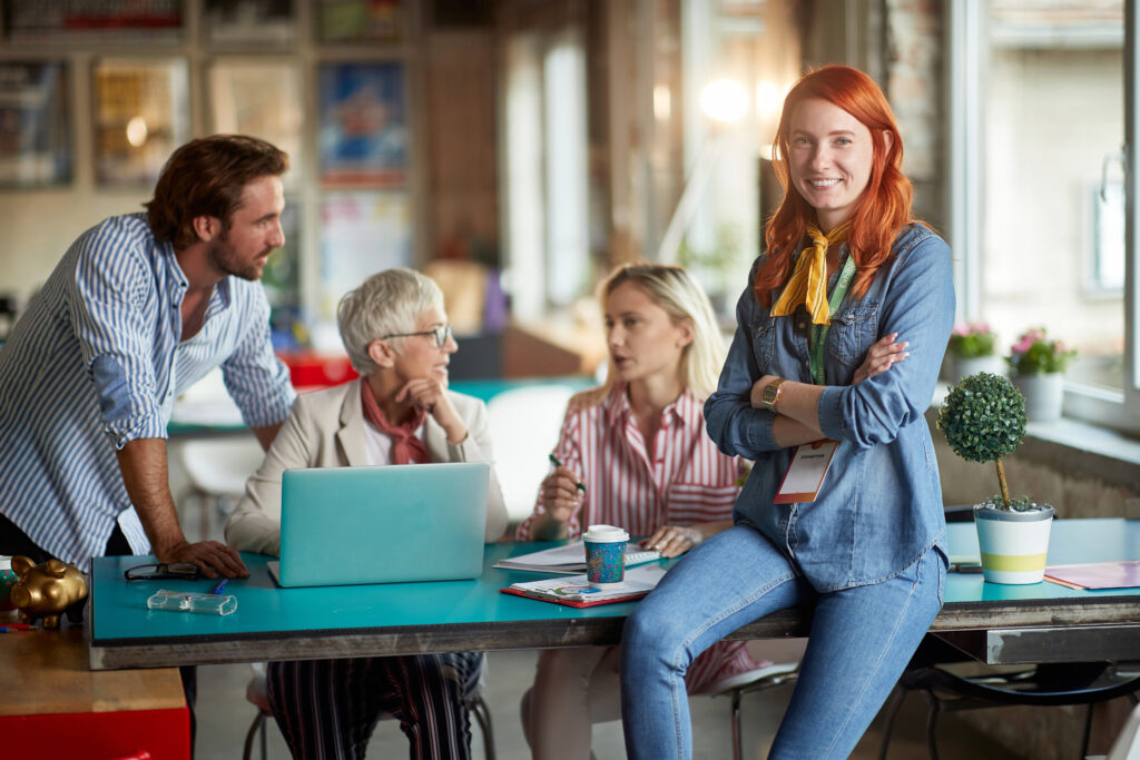 A young beautiful woman is posing for a photo while enjoying a work with her colleagues in a relaxed atmosphere in the office