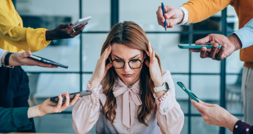 Shot of a stressed out businesswoman surrounded by colleagues needing help. Businesswoman feeling stressed out in a demanding office environment at work. Photo of businesswoman under strain as colleagues request various things from her. Businesswoman feeling overwhelmed by her colleagues in the office. Frustrated businesswoman having a headache while her colleagues are demanding her to work on many things in the office. Stress, anxiety and multitasking businesswoman with headache from workload and laptop deadline in office.